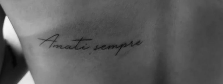 Fotografia in bianco e nero di un tatuaggio minimalista in corsivo sulla schiena con le parole 