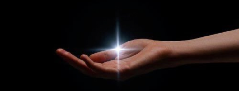Immagine concettuale della Legge dell'Attrazione: una mano aperta e rivolta verso l'alto, immersa nel buio, su cui si accende un punto di luce brillante che simboleggia l'accensione di un'idea, di un pensiero focalizzato o l'inizio del processo di manifestazione.