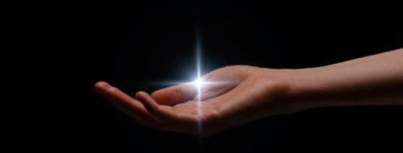 Immagine concettuale della Legge dell'Attrazione: una mano aperta e rivolta verso l'alto, immersa nel buio, su cui si accende un punto di luce brillante che simboleggia l'accensione di un'idea, di un pensiero focalizzato o l'inizio del processo di manifestazione.